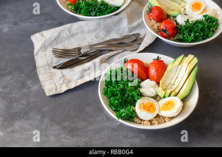 Le quinoa cuit avec des bols de bouddha les tomates, l'avocat, le chou vert, œufs durs et du yaourt grec sur fond de béton gris. Petit déjeuner sain. Banque D'Images