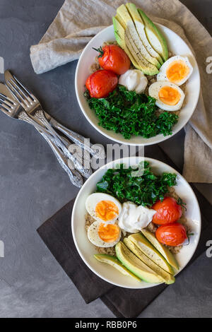 Le quinoa cuit avec des bols de bouddha les tomates, l'avocat, le chou vert, œufs durs et du yaourt grec sur fond de béton gris. Petit déjeuner sain. Vue d'en haut. Banque D'Images