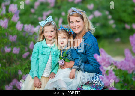 Mère femme avec deux sœurs filles souriant mignon joli ensemble sur un champ de lilas bush qui portaient tous des robes et manteaux jeans élégant Banque D'Images