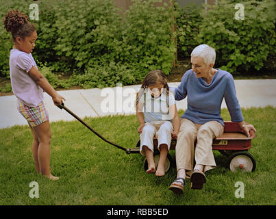 Grand-mère assise dans un panier tout en s'amusant avec ses deux petites-filles dans la cour avant. Banque D'Images