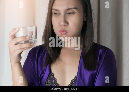 Asian Woman in lingerie de soie et de soie robe pourpre de l'eau de boisson contre un arrière-plan gris, les gens et en se gargarisant de rinçage lors de l'utilisation d'un rince-bouche Banque D'Images