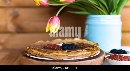 Des crêpes pour les vacances de printemps russe traditionnel. Crêpes minces avec du caviar rouge et noir et un bouquet de tulipes. Fond de bois et fest Banque D'Images