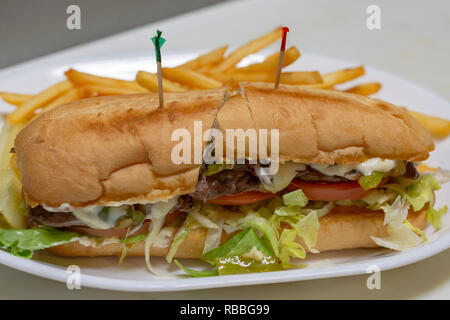 Philadelphia cheesesteak sandwich sur un sous bun. Plateau blanc avec des cure-dents. De moitié. Frites en arrière-plan. Banque D'Images