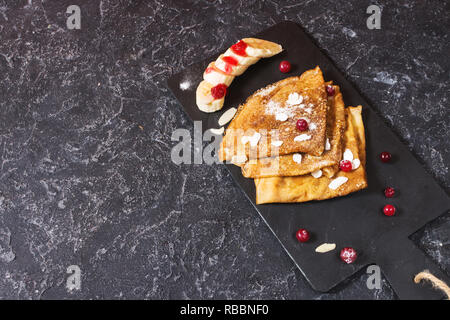 Crêpes traditionnelles de banane et fruits rouges sur fond noir en noir. Copy space Banque D'Images
