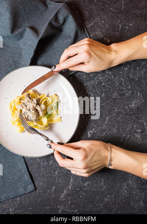 Pâtes aux champignons et sauce sur fond noir en noir. Les mains tiennent le couteau et la fourchette Banque D'Images