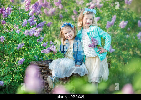 Deux soeurs filles souriant mignon joli ensemble sur un champ de lilas bush qui portaient tous des robes et manteaux jeans élégant Banque D'Images