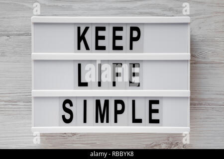 "Simplifier la vie" mots sur conseil moderne blanc sur fond de bois, vue du dessus. Mise à plat, d'en haut. Banque D'Images