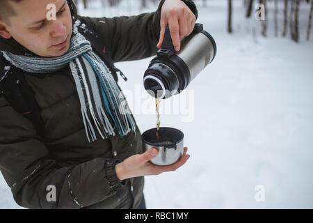 L'homme élégant verser le thé chaud d'un thermos dans une forêt de pins. Banque D'Images