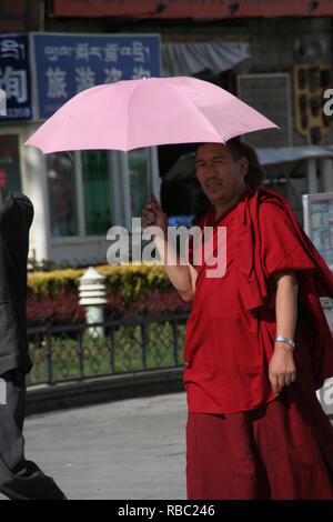 Moine tibétain en robes rouges portant un parapluie rouge sur sa tête pour le protéger du soleil en altitude au pied de l'Himalaya, au Tibet, Chine Banque D'Images