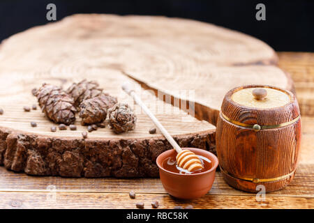 Canon avec du miel et du miel stick sur un fond de bois avec des pommes de pin couché sur un trait de scie. Produits du bois texturé. Close-up. Banque D'Images