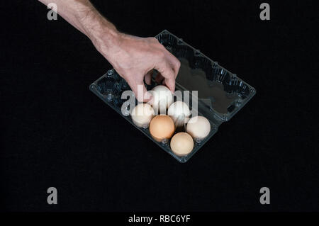 La main des hommes en tenant un oeuf de l'oeuf en plastique fort sur fond de feutre noir. Banque D'Images