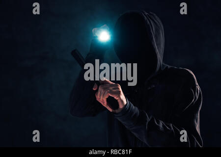 Les vols à main armée, criminel avec hoodie holding gun et retraite aux flambeaux et d'attaquer dans l'obscurité, selective focus low key Banque D'Images