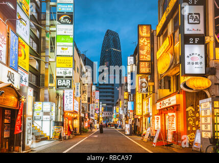 Shinjuku, Tokyo, région du Kanto, au Japon. Enseignes au néon lumineux au crépuscule et Cocoon Tower en arrière-plan. Banque D'Images