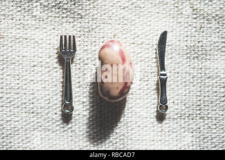 Un haricot, fourchette et cuillère miniature sur nappe. Banque D'Images