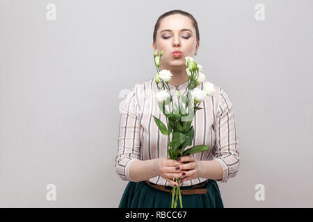 Portrait of attractive young woman in charmant romantique chemise rayée et jupe verte holding bouquet de fleurs blanches et d'envoi de la baiser. Piscine, le stu Banque D'Images