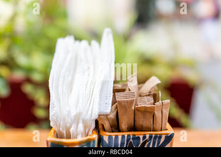 Gros plan du sel, poivre et sucre brun en paquets contenant sur tableaux tableau dans un café restaurant en plein air à l'extérieur terrasse patio, plantes vertes et blanches Banque D'Images