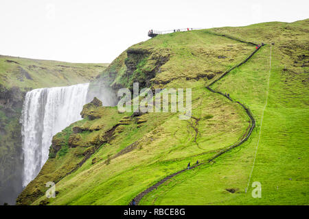 Skogafoss, chute d'Islande sur falaise avec Green Grass Hills et de nombreux touristes qui marchent sur des sentiers en haut de la route d'été moussu Banque D'Images