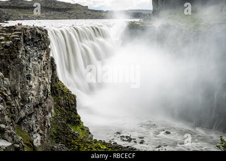 Cascade de Dettifoss en Islande islandais longue exposition de l'eau lisse gris en mouvement et une falaise rocheuse de la pulvérisation et les gens se tenant loin sur donnent sur Banque D'Images