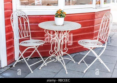 Table en métal blanc vide à l'extérieur restaurant café avec deux chaises sur le trottoir et dans la rue des fleurs orange pot de plante en pot avec personne ne par Banque D'Images