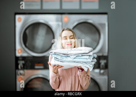 Young woman enjoying nettoyer des vêtements repassés dans l'auto lavage auto buanderie avec sèche-linge automatiques sur l'arrière-plan Banque D'Images