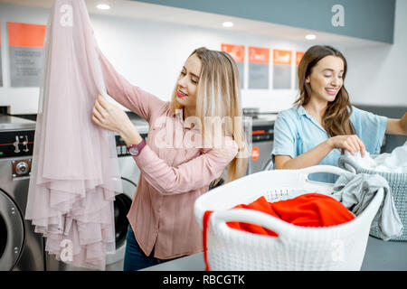 Deux amies gaies vêtements tri pour laver debout dans la blanchisserie en libre service Banque D'Images