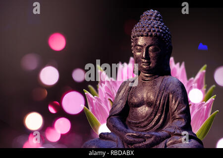 Statue de Bouddha assis en méditation poser contre fond sombre et fleur de lotus rose derrière. Banque D'Images