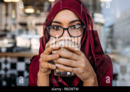 Close up portrait of young woman wearing hijab et lunettes de boire du café. Femme musulmane ayant une tasse de café au café. Banque D'Images