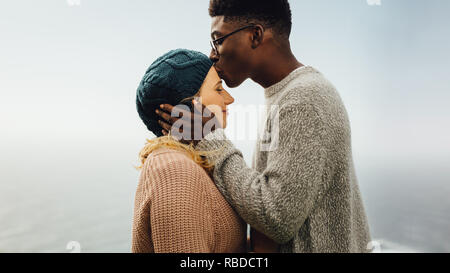 Vue de côté d'aimer l'interracial couple ensemble à l'extérieur. Jeune homme embrassant le front de sa petite amie. Banque D'Images