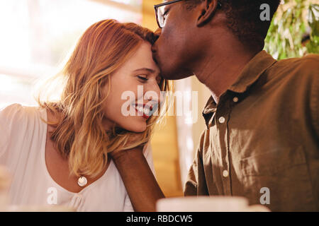 Homme africain s'embrasser le front de sa petite amie. Loving couple interracial le date à café. Banque D'Images