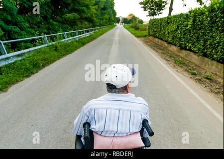 Vue de derrière du vieil homme à l'extérieur en fauteuil roulant avec une longue ligne droite de l'avant, symbole de l'avenir de la vie ou de métaphore pour les progrès de la médecine Banque D'Images