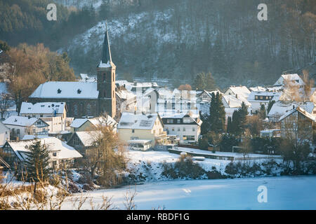 Vue sur le lac gelé de Rursee l'église et village de Einruhr avec de la neige en hiver, dans l'Eifel, en Allemagne. Banque D'Images