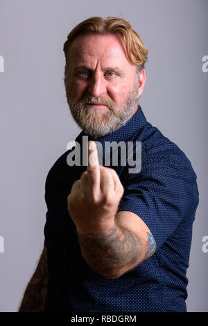 Homme barbu d'âge mûr avec des tatouages main montrant doigt moyen Banque D'Images