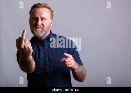 Homme barbu d'âge mûr avec des tatouages main montrant doigt moyen Banque D'Images