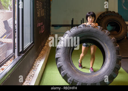 Asian woman flipping et remise en forme de pneus de camion roue at gym Banque D'Images