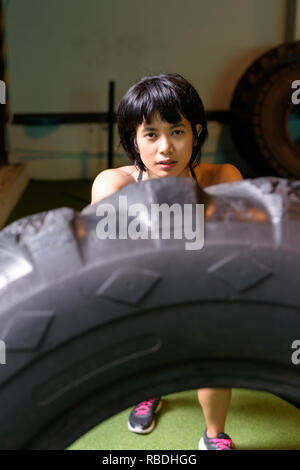 Asian woman flipping et remise en forme de pneus de camion roue at gym Banque D'Images