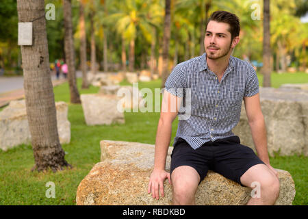 Portrait de jeune homme assis beau et relaxant au parc Banque D'Images