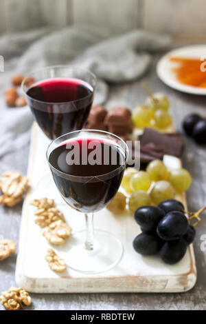 Crème de Cassis liqueur maison servi avec des raisins, noix et chocolat. Style rustique. Banque D'Images