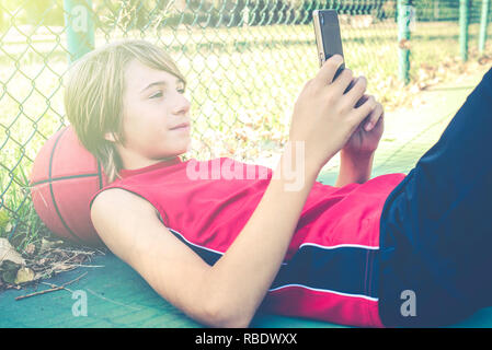 L'adolescent smartphone avec des amis pour jouer au basket-ball en plein air - sportive saine vie adolescents concept Banque D'Images