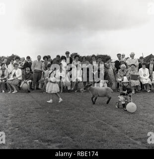 1967, historiques, à l'extérieur à une fête du village, une aire pour enfants robe de compétition, les spectateurs assis à regarder une jeune fille comme 'little bo peep', à la tête d'une petite brebis. Le personnage est une comptine anglaise populaire sur une jeune bergère. Banque D'Images