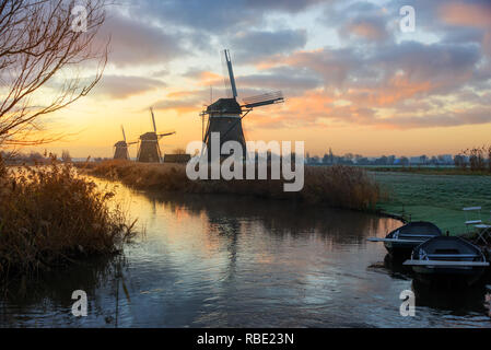 Trois moulins à vent, deux chaloupes et un canal dans un paysage rural à Leidschendam, Pays-Bas au lever du soleil en hiver. Banque D'Images