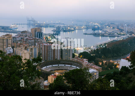 La ville espagnole de Malaga dans la soirée. Port et de la vieille ville avec un anneau de taureau ci-dessus. Les bâtiments et les navires dans le port peut être vu à l'arrière. Banque D'Images