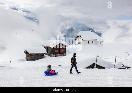 L'enfant sur une luge admire les refuges de montagne couverte de neige Bettmeralp Française, canton du Valais Suisse Europe Banque D'Images