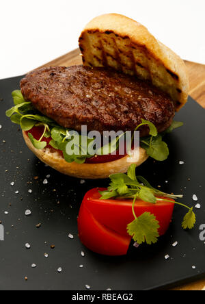 Juteux et succulent burger de boeuf rare, avec tomate et garnir de cresson, dans un pain bun, sur une plaque en ardoise Banque D'Images