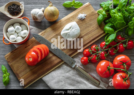 Cuisine italienne. Planche à découper en bois entouré par la cuisson ingrédients, légumes et fromage mozzarella sur fond gris. Banque D'Images