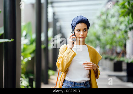 Une jeune et belle femme du Moyen-Orient dans un turban hijab fronce comme elle parle sur son smartphone dans la rue pendant la journée. Elle a l'air inquiet. Banque D'Images