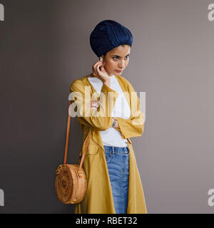 Portrait d'un jeune, élégante et belle femme du Moyen-Orient dans un turban hijab foulard et élégant sur le thème pastel les vêtements. Banque D'Images