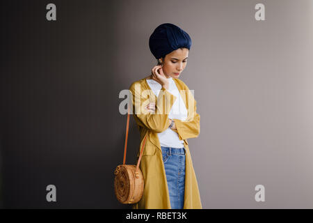 Portrait d'un jeune, élégante et belle femme du Moyen-Orient dans un turban hijab foulard et élégant sur le thème pastel les vêtements. Banque D'Images