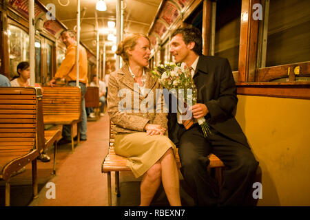 Mid-adult man holding a bouquet de fleurs tout en étant assis à côté de sa petite amie dans un train. Banque D'Images