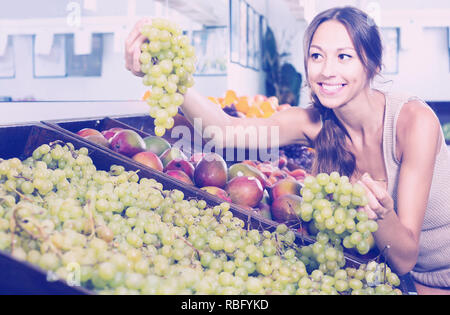 Jeune femme espagnole positive Le choix du client en magasin fruits raisins Banque D'Images