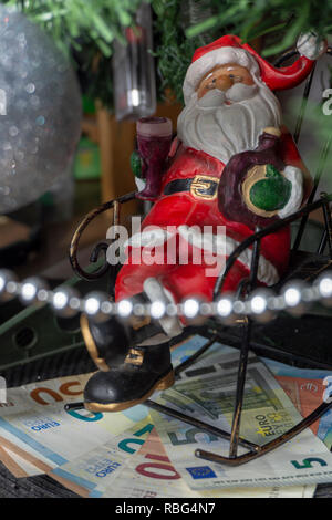 Santa Christmas ornament brûlée dans une chaise en métal dans le cadre d'un Noël avec des billets en euros en une image conceptuelle Banque D'Images